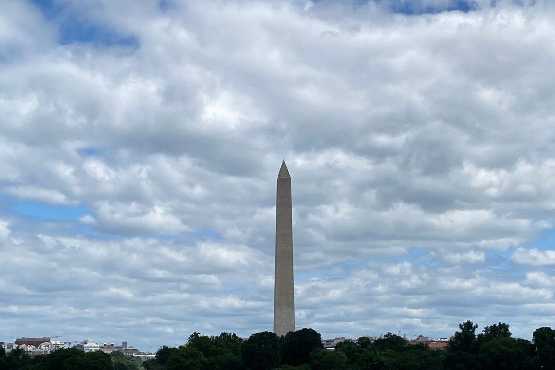 Washington Monument rising above green summer trees along the Potomac