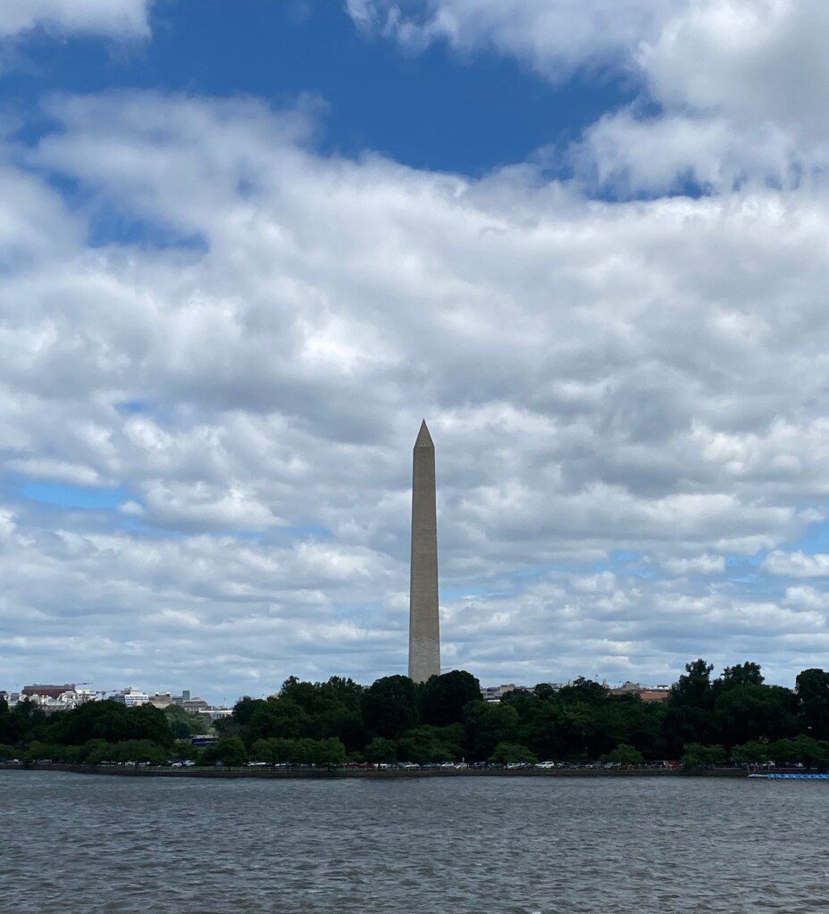 Washington Monument rising above green summer trees along the Potomac